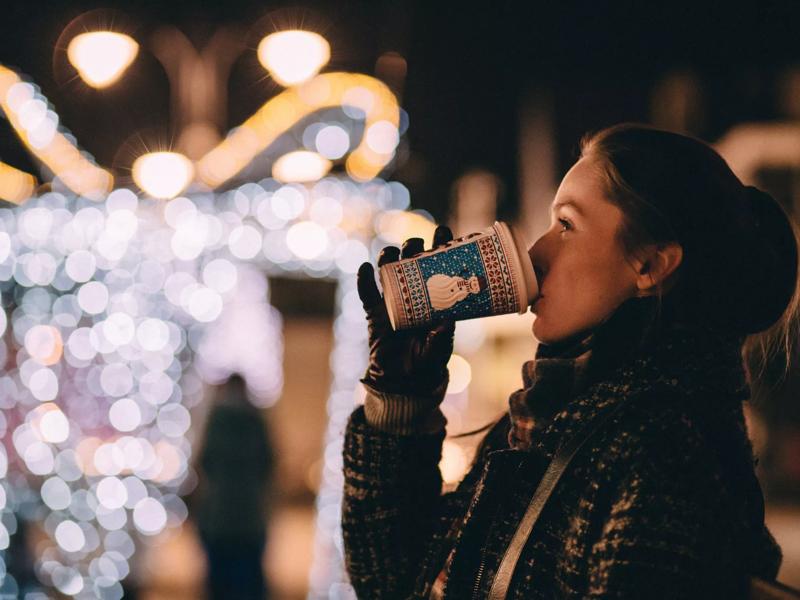 woman sipping coffee with holiday lights