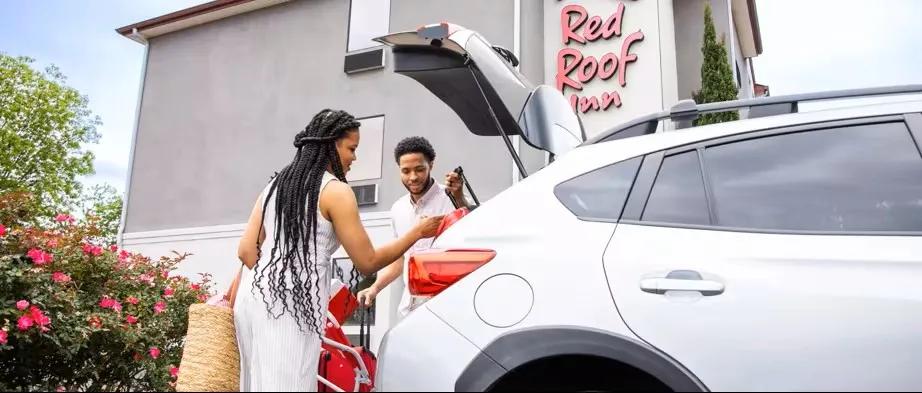 Family unpacking luggage from car in front of a Red Roof Inn