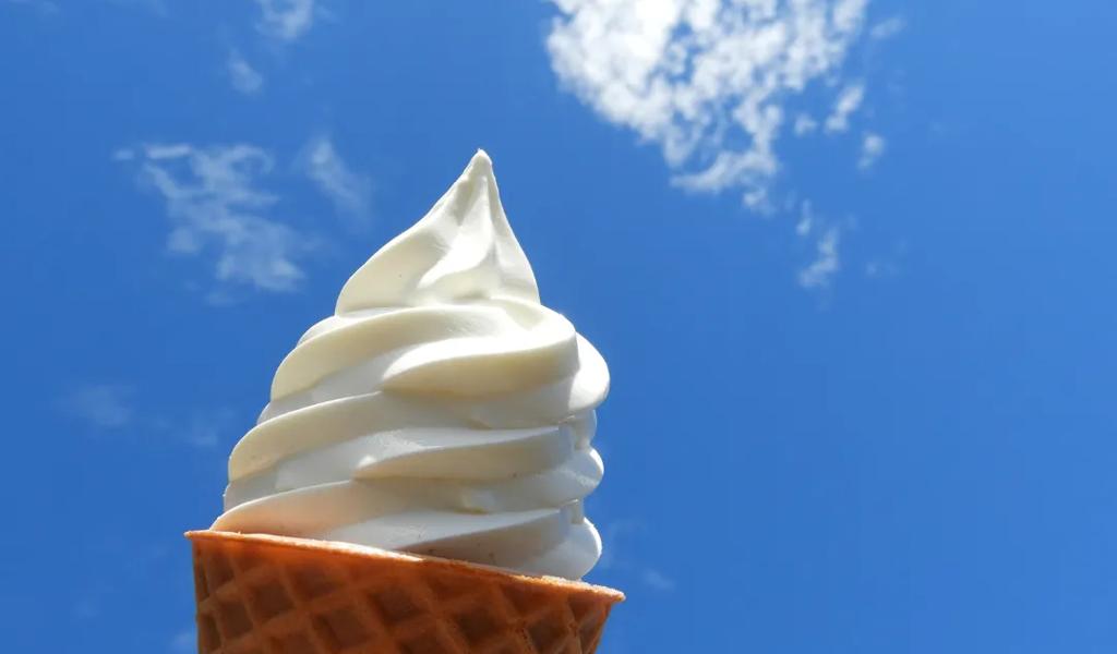 A vanilla soft serve ice cream cone held up to the sky