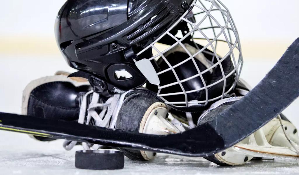 Hockey helmet, stick, and puck lying on the ice in a rink.