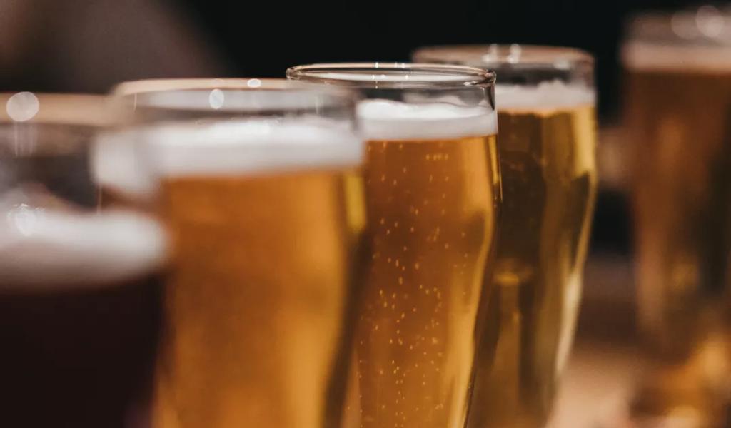 A row of glasses filled with various beers on a wooden table