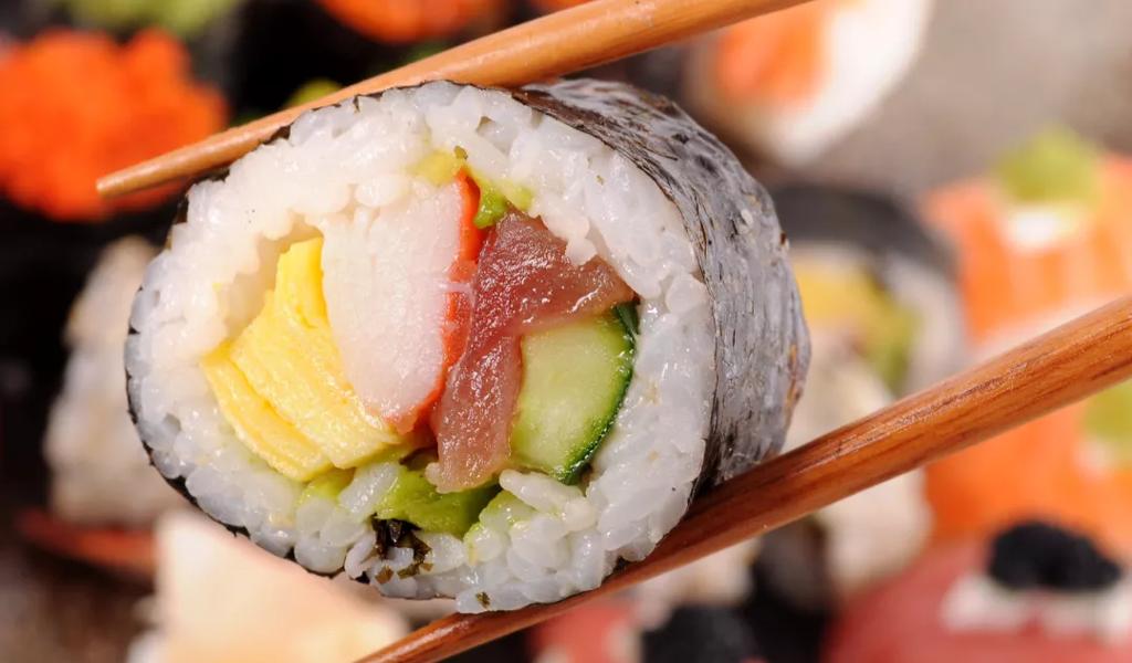 Close-up of sushi roll held by chopsticks